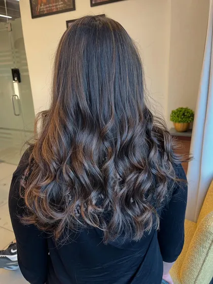 A back view of a client's hair after a balayage and styling session. The curls are defined and the color looks rich.