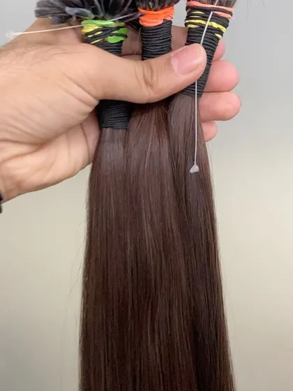 A hand holding several bundles of our brown I-Tip extensions, ready for a custom installation.