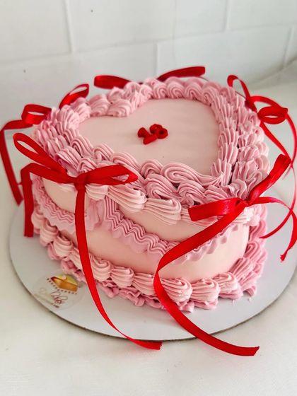 A romantic heart-shaped cake with vintage piping and delicate red ribbons.