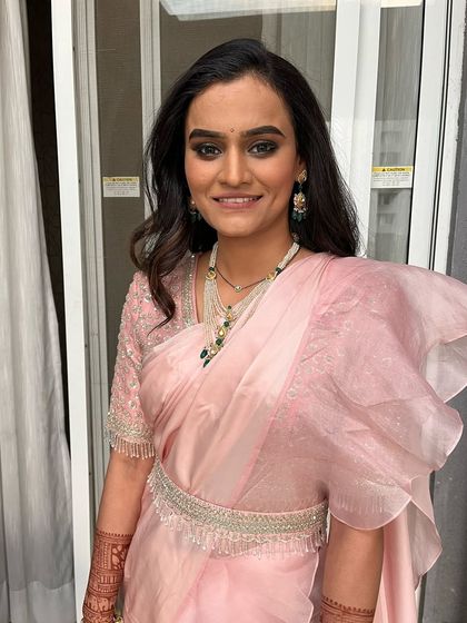 A smiling portrait of the bride in her reception attire. The soft pink saree and modern jewelry are paired with a bold eye and natural lip.