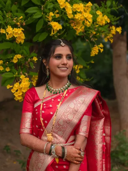 A beautiful portrait of the bride, showcasing her complete reception attire. The soft lighting highlights the intricate silver work on her red saree and the emerald green of her jewelry.