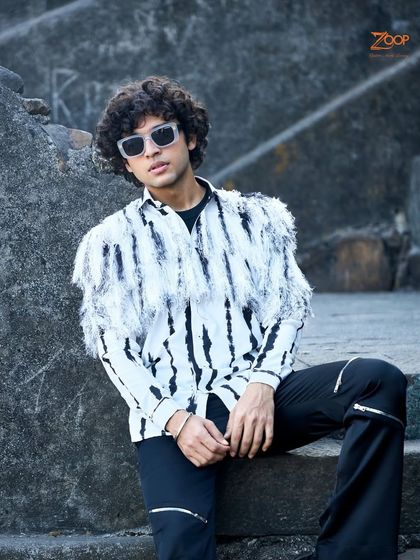 This look is for the bold. A black and white tie-dye effect shirt with fringe detailing on the shoulders, paired with black trousers with zipper details, creates an edgy, high-fashion look.