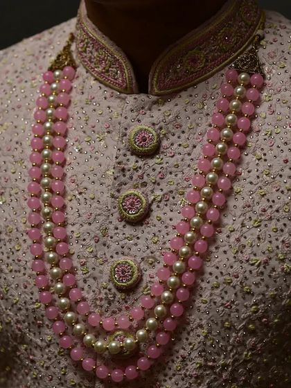 A detailed shot of the beautiful buttons and the layered pearl and pink bead necklace, which adds a modern touch to this traditional pre-loved sherwani.