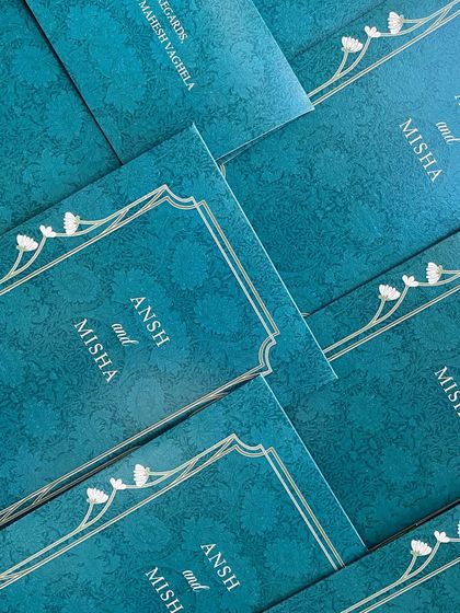 A stack of stunning teal invitation folders. The rich color and damask pattern, paired with a simple, elegant border, create a look of modern royalty.
