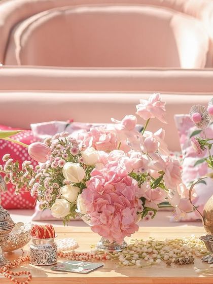 A close-up of a coffee table arrangement, featuring pink hydrangeas and tulips in antique silver and brass vases.