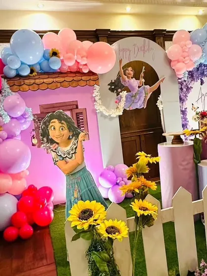 A magical Encanto themed party setup with character cutouts, a house facade, and vibrant balloon and flower decorations creating a lively scene.
