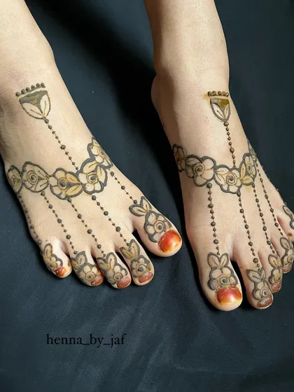 A delicate and symmetrical henna design for the feet. This pattern resembles a traditional anklet, with floral chains draping beautifully over the top of the feet and toes.