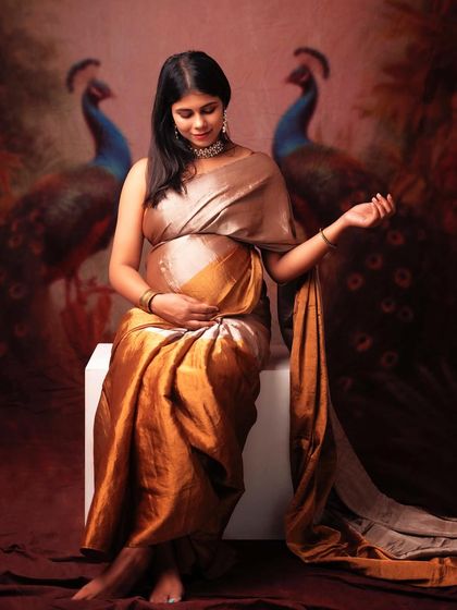 A regal portrait of a mom-to-be in a golden saree, with a painterly peacock background. This is a classic and artistic way to celebrate your pregnancy.