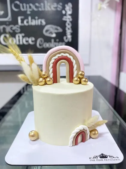 A minimalist boho-chic cake with fondant rainbows, pampas grass, and gold spheres.