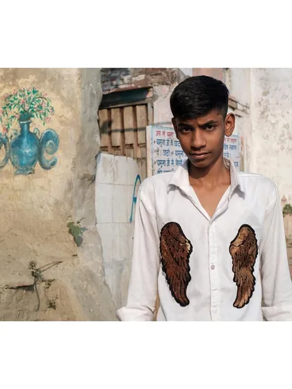 A young man in a shirt adorned with angel wings, shot against a rustic wall in Delhi. The juxtaposition of modern fashion and the old, textured background creates a compelling street portrait.