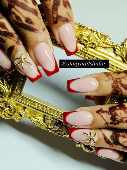 Simple yet festive red French tips paired with henna-adorned hands. This classic look is elevated with a delicate gold bow charm, making it perfect for any celebration.