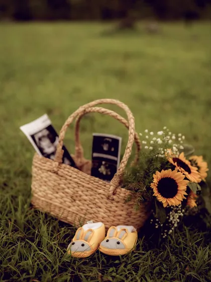 The little details that tell a big story. A picnic basket with sunflowers, sonogram pictures, and adorable baby bunny shoes, all set in a beautiful green field.