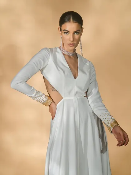 A close-up of a white long-sleeved gown with cut-outs from the 'Ivory Edit'. The pose highlights the sleeve details and the modern silhouette of the dress.