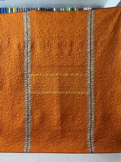 This reversible memory quilt was crafted from a mother's sarees, featuring a vibrant orange side with silver zari borders.