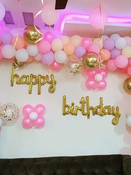 An elegant pastel balloon arch against a plain wall. This organic garland uses shades of pink, purple, and peach, with gold chrome balloons and 'Happy Birthday' foil letters for a sophisticated look.