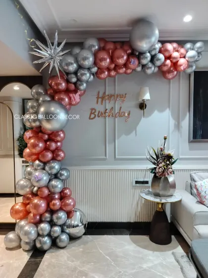 This elegant birthday balloon arch is perfect for a sophisticated home party. We use a mix of rose gold and silver chrome balloons in various sizes, with a starburst foil balloon accent, to frame your celebration space beautifully.