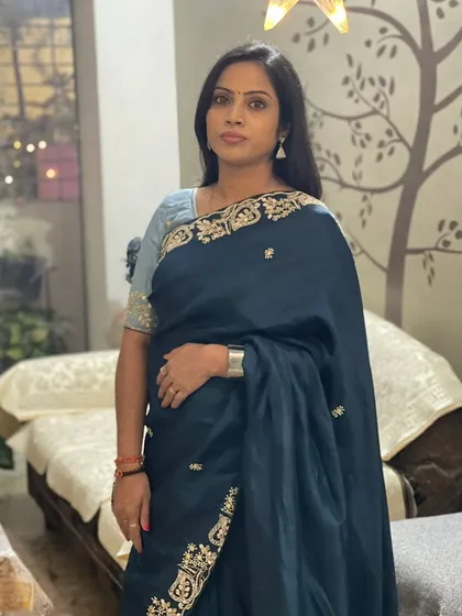 A client looking elegant in a deep teal blue saree with a gold embroidered border, paired with a contrasting light blue blouse.