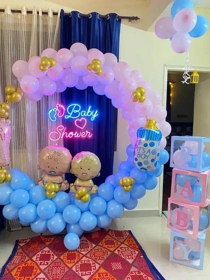 For this baby shower, I created a whimsical crescent moon balloon arch using pastel pink and blue balloons. The design includes baby-themed foil balloons and transparent 'BABY' boxes to complete the look for the celebration at home.