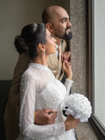 A pensive and artistic wedding portrait of the couple looking out a window. The natural light creates a soft, romantic mood.
