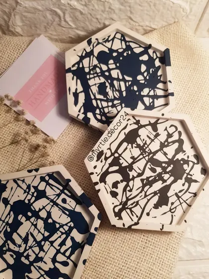A set of three hexagonal coasters with a modern, abstract black paint splatter design.