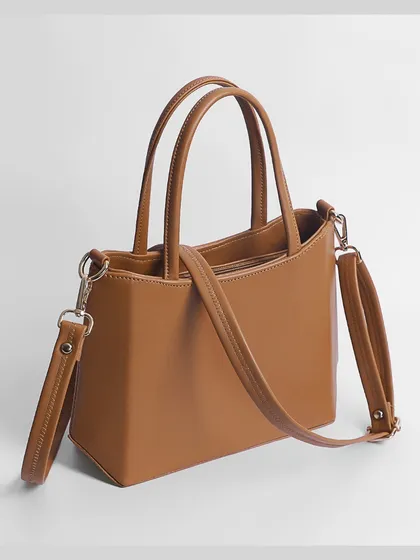 A three-quarter view of a tan handbag with its shoulder strap attached, showing its versatility.