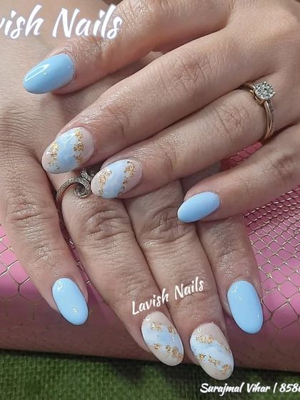 A lovely pastel blue set with accent nails featuring a nude base, blue watercolor patches, and gold foil flakes.