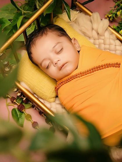 A close-up of the baby in the "Jai Shree Ram" setup, wearing a saffron wrap and a rudraksha necklace. The details are key to making these themes special.