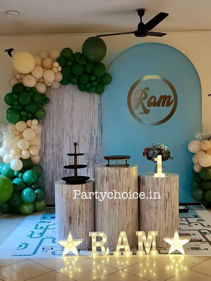 A simple and stylish birthday setup for a boy's first birthday. The decor uses a clean color palette of green and white, with log-themed plinths and a personalized backdrop.