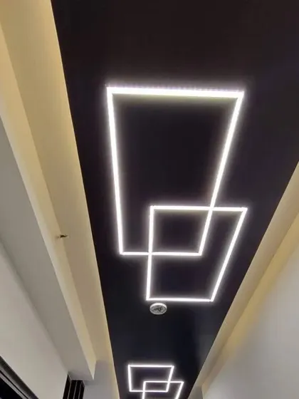 A long corridor ceiling with interlocking square patterns made from profile LEDs. The black background makes the white light pop, creating a high-contrast, futuristic look.