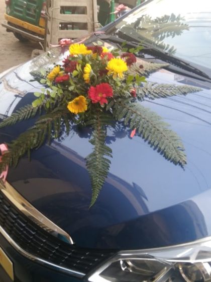A simple bouquet of colorful flowers and ferns placed on the bonnet of a blue car. This is a great example of a minimal yet beautiful car decoration.
