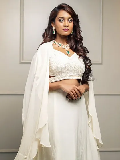 For a modern and chic statement, we offer this white fusion lehenga set. The intricately embroidered crop top is paired with a simple skirt and a dramatic, flowing cape for a truly contemporary ethnic look.