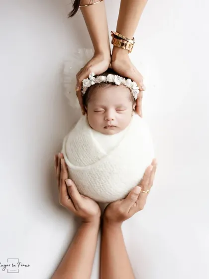 A creative newborn portrait where the baby is held safely between the mother's and father's hands. The mother's bangles and father's ring add a personal touch.