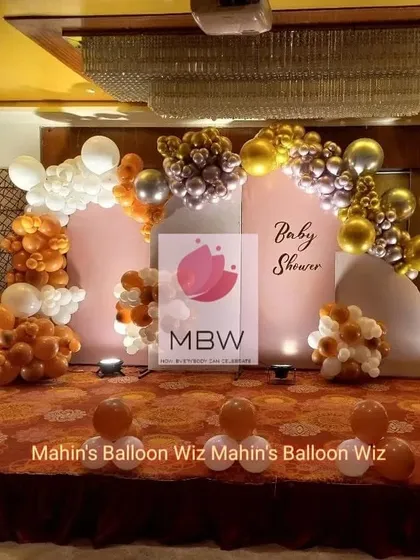 A chic and modern baby shower design using a warm, earthy palette of orange, brown, and metallic balloons. The simple arched backdrops create an elegant and contemporary look.