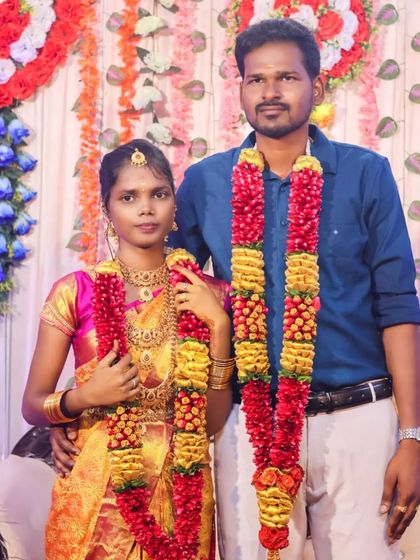 A classic posed portrait of the couple on their wedding day. They stand together adorned with heavy garlands, a timeless photograph that is a must-have for any wedding album.