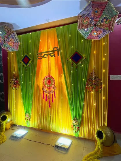 This is a classic Haldi ceremony backdrop I created. It uses vibrant yellow and green drapes, traditional embroidered umbrellas, and decorative earthen pots overflowing with marigold flowers for an authentic feel.