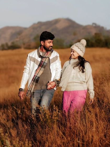An expecting couple walks hand in hand through a rustic field, their comfortable winter outfits adding to the cozy, natural feel of the moment. I encourage simple, candid actions like walking and talking to capture authentic connection.