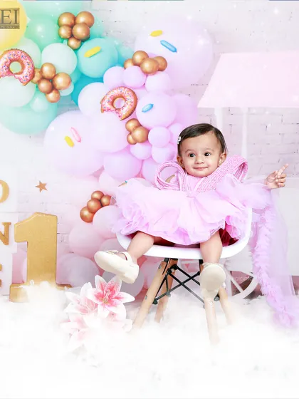 Dressed in pink, this little girl is the star of her donut-themed first birthday shoot. The vibrant balloon arrangement adds a festive touch to her milestone portrait.