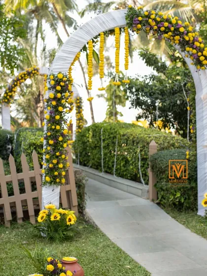 A charming walkway with floral arches leading to the Haldi event. The combination of white structures and bright yellow marigolds creates a cheerful and inviting path for guests.