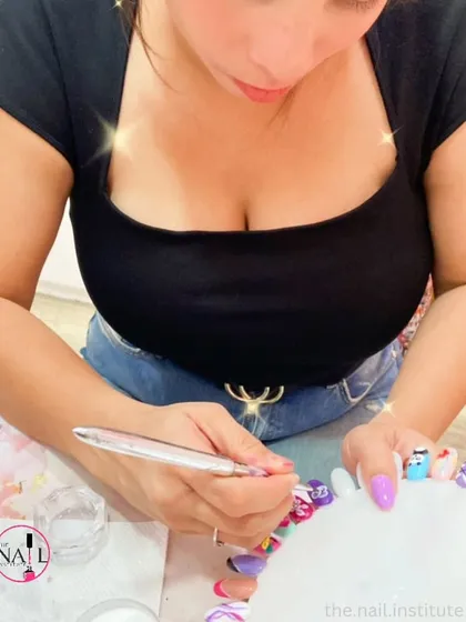 This student is practicing 3D nail art, adding colorful details to a practice nail tip.