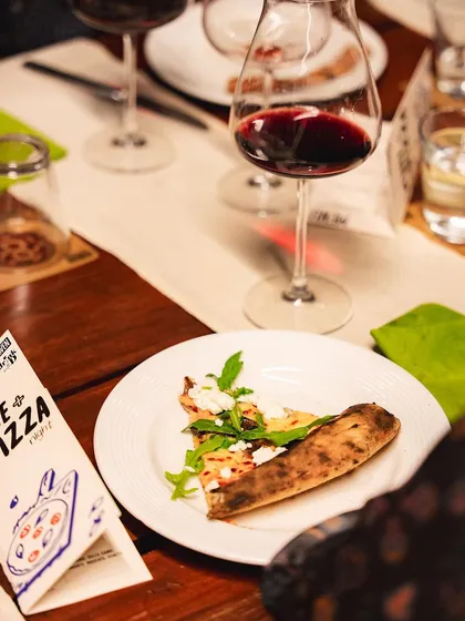 A slice of pizza paired with a glass of red wine at our Wine + Pizza Night. We work with experts to create perfect pairings.