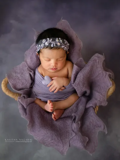 Nestled in a basket, this newborn baby girl wears a lovely embroidered headband. The soft purple tones and dreamy background create a truly magical and serene portrait.