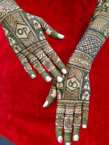 A close-up of an engagement mehendi with the couple's initials 'OP' and interlocking rings, set within a grid-like pattern.