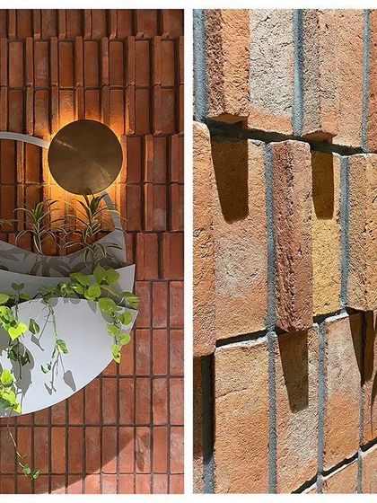 This biophilic art piece on an atrium wall depicts the dawn sky. The custom planter symbolizes the earth, the curves suggest the wind, and a brass disc represents the rising sun, all set against a textured brick wall.