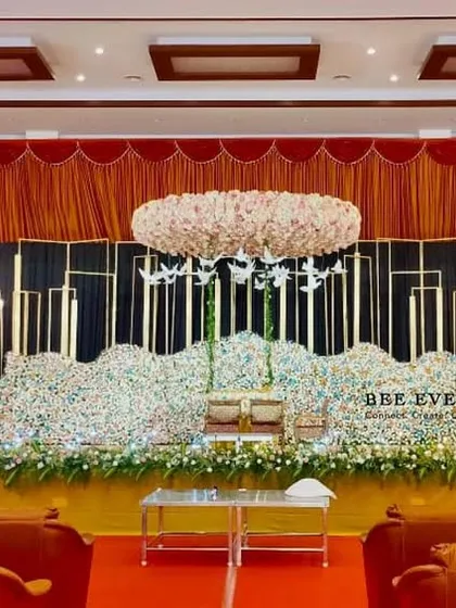 A wide-angle view of a breathtaking reception hall we decorated. The stage features a massive floral base, a stunning overhead floral chandelier, and elegant candle-like lighting, creating a truly grand and immersive experience.