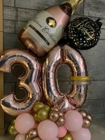 A stylish balloon bouquet for a 30th birthday. This arrangement features rose gold '30' foil numbers, a large champagne bottle foil balloon, and a base of pink and chrome gold balloons.