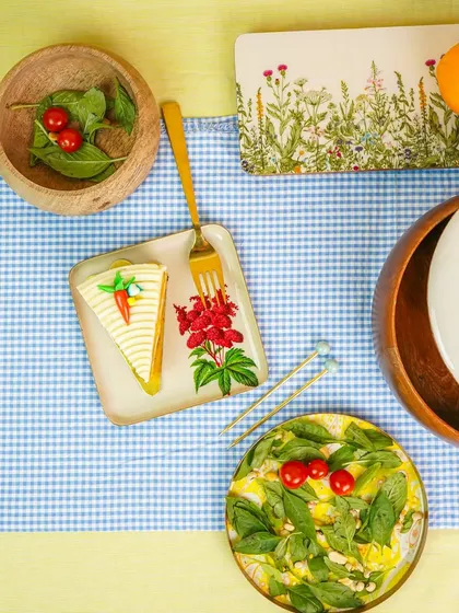 A top-down view of a picnic-style table setup with patterned plates, a wooden bowl, and fresh food items.