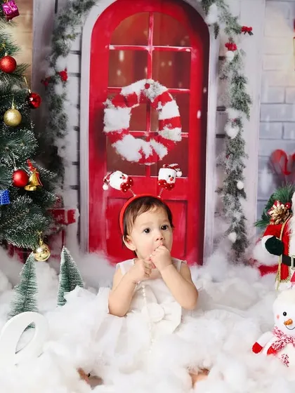 A wider view of the Christmas first birthday setup, showing the little girl surrounded by a tree, snowman, and candy canes.