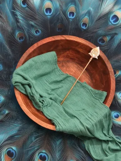 A stunning prop setup for a Muruga or peacock theme, featuring a wooden bowl and a small spear on a bed of vibrant peacock feathers.