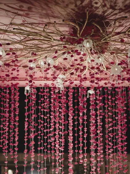 A wider view of the custom ceiling installation, showing the interplay between the golden branches, crystal lamps, and the dense curtain of pink floral strings. This created a dreamy, romantic atmosphere for the night ceremony.