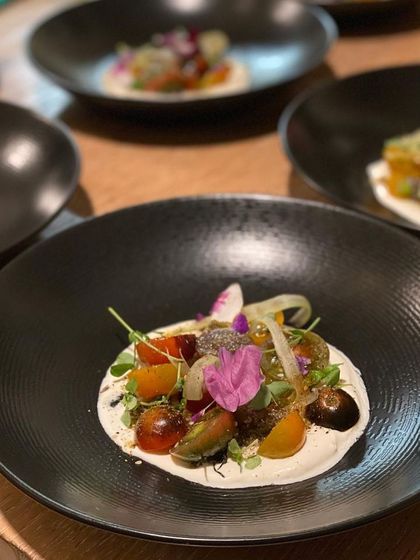 A fresh and vibrant tostada with heirloom tomatoes, herbs, and a creamy base, served on a dark plate to highlight its colors.
